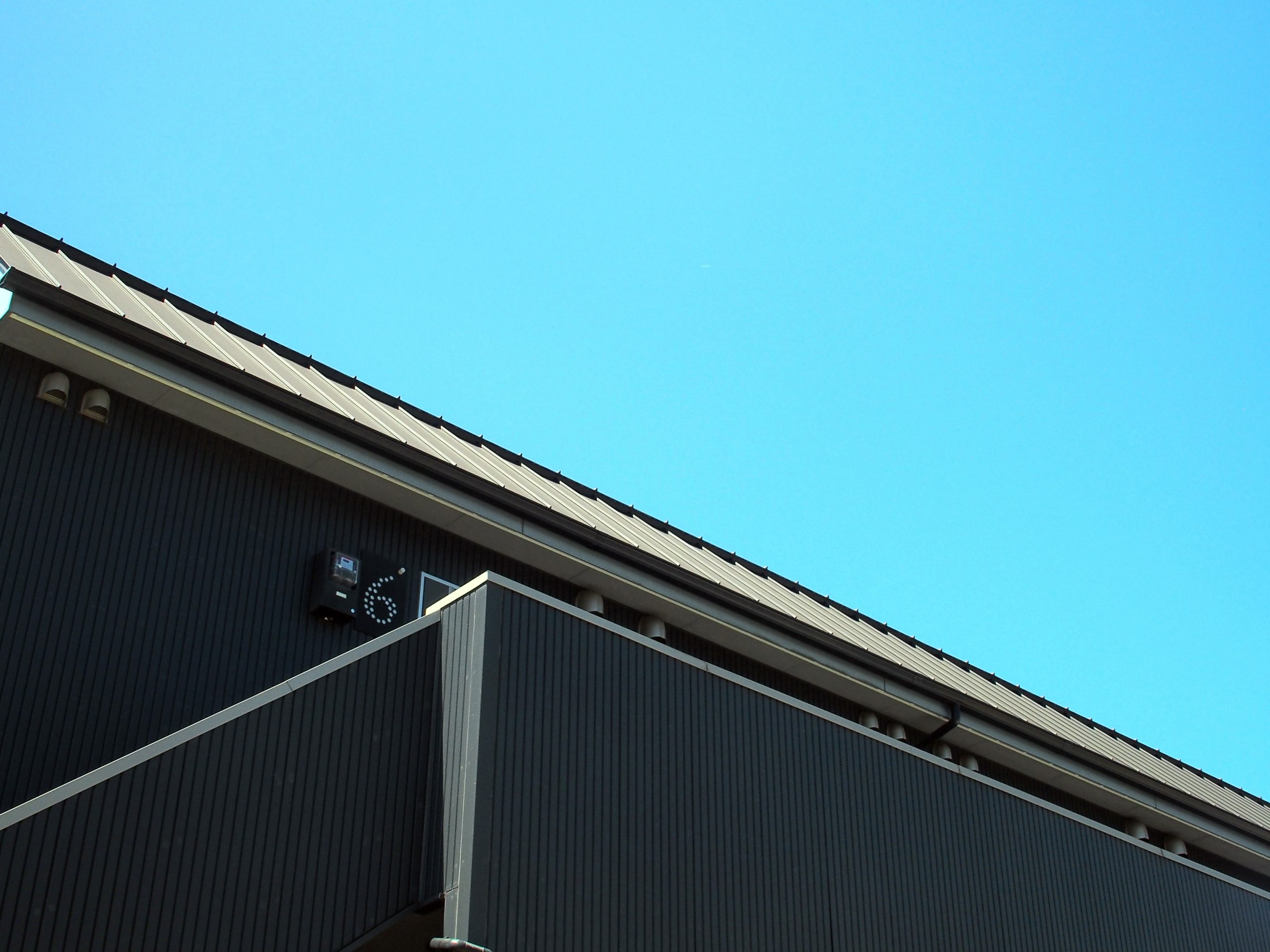 下から見たアパートの黒い壁と屋根。背景は夏の青空