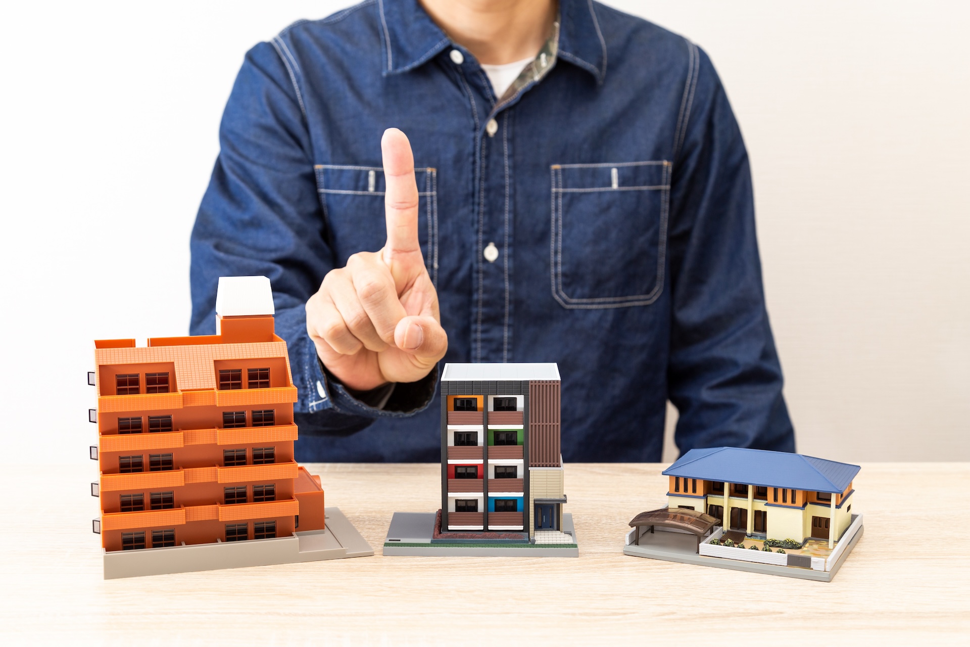 マンション、アパートなどの住宅模型の前で1を示す男性