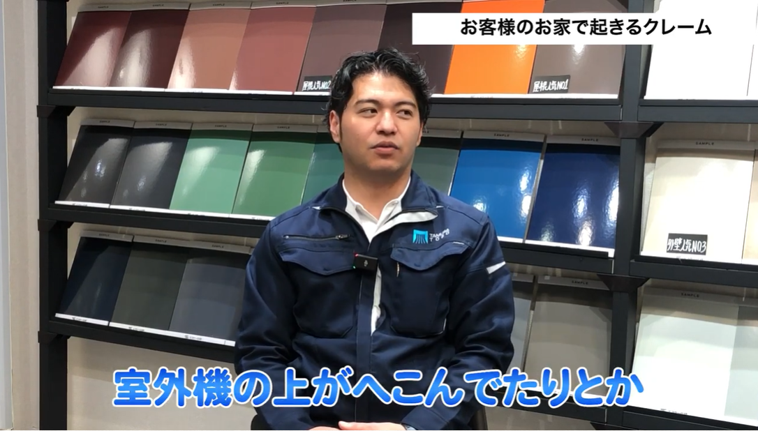 塗装専門店のスタッフが、施主からのクレーム事例として「室外機がへこんでいた」という物損事故について解説している場面。職人が足場代わりに室外機に乗ってしまうなどの原因と、養生や注意喚起といった再発防止策の重要性を説明している。