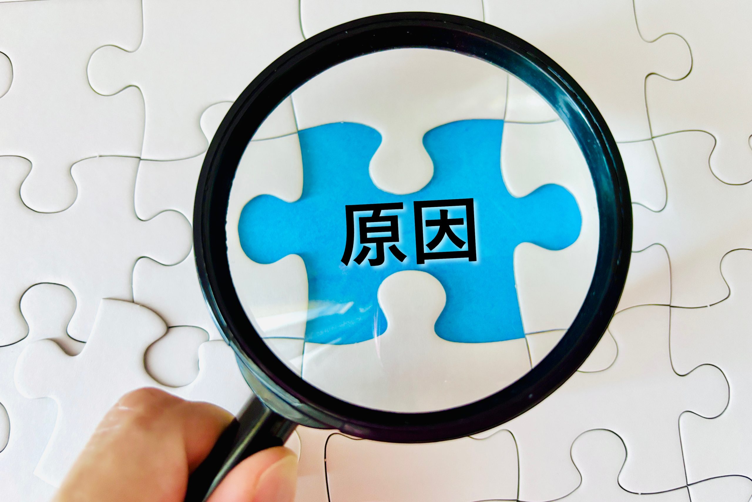 「原因」と書かれた青いパズルピースを虫眼鏡で覗き込んでいる様子